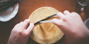 a vanilla bean being sliced open on a wooden cutting board with a knife