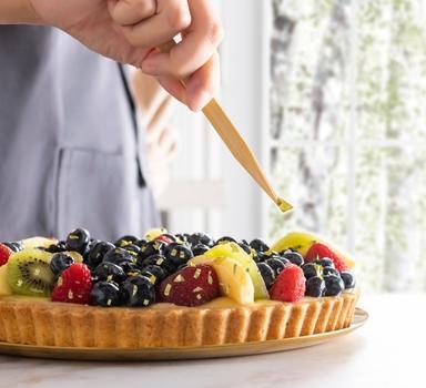 Person adding edible gold leaf to a fruit tart