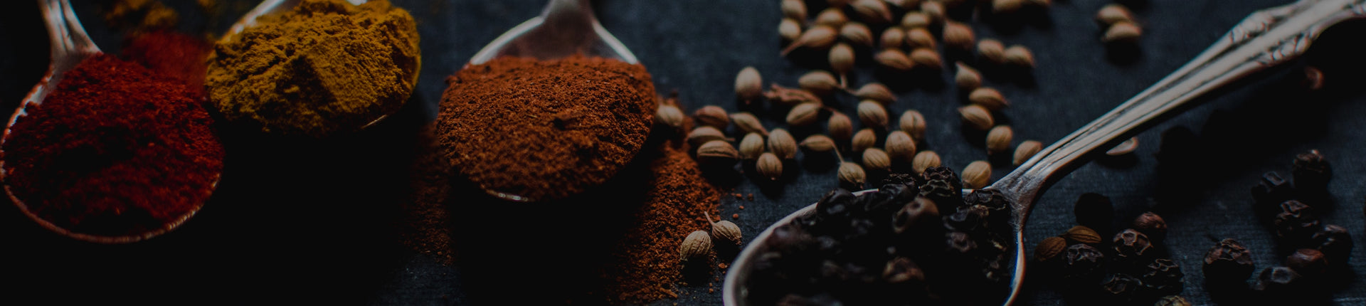 Spice of chili powders, peppercorns and coriander in silver spoons on a dark counter top