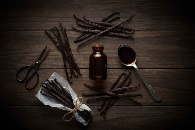 Vanilla beans, a bottle, and a spoon on a wooden surface
